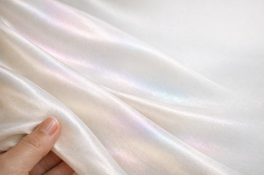 A close-up of ivory mulberry silk fabric held to the light, its color-shifting sheen and fine weave revealing it as real silk