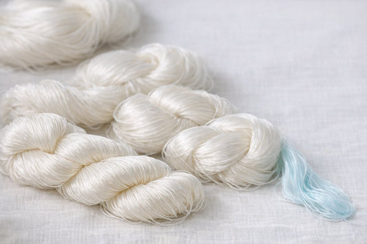 Skeins of pearly-white raw mulberry silk thread in soft natural light, their long even fibers and clean luster visible